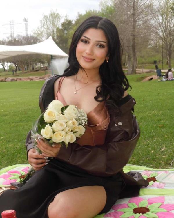 A young woman sitting on a blanket holding a bouquet of flowers, identified as Muna Pandey, a 21-year-old student from Houston Community College.